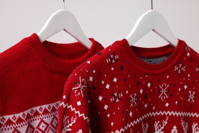 Christmas sweaters hanging on rack against light background, closeup