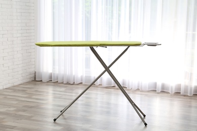 Modern empty ironing board near window at home