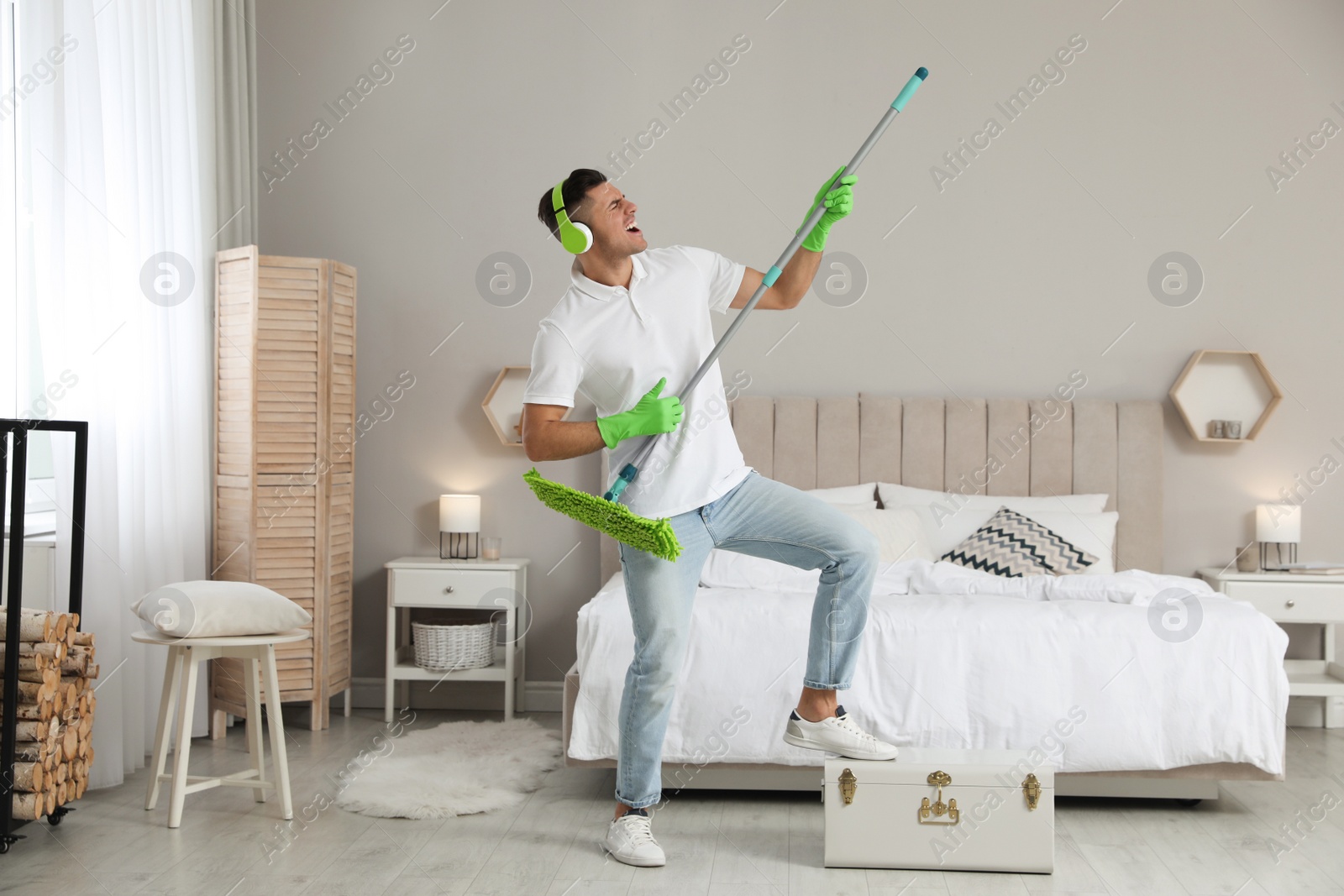 Photo of Man with mop singing while cleaning in bedroom