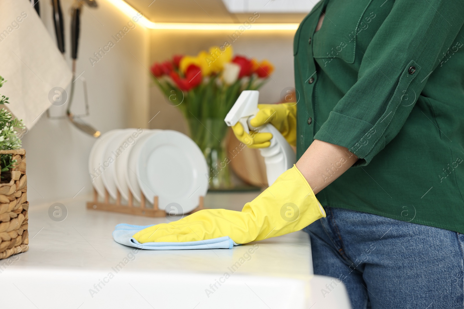 Photo of Woman cleaning furniture with rag and spray bottle in kitchen, closeup