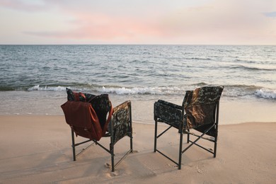 Photo of Camping chairs and backpack on sandy beach near sea