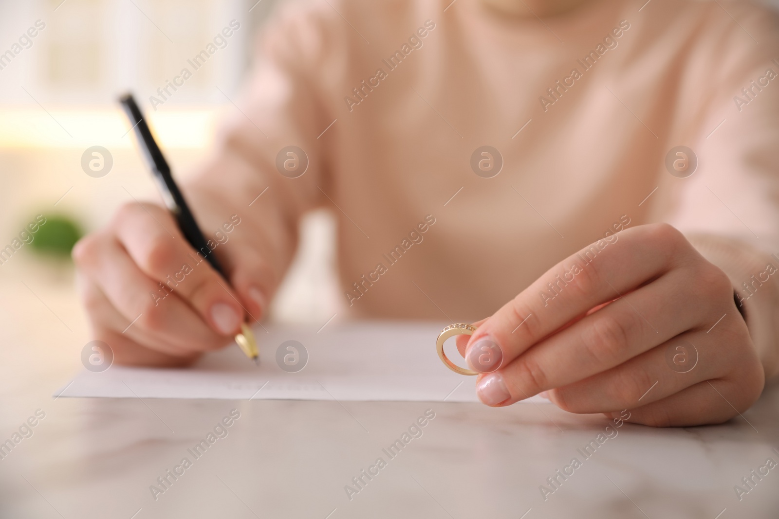 Photo of Woman with wedding ring signing divorce papers at table indoors, closeup