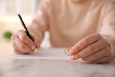 Photo of Woman with wedding ring signing divorce papers at table indoors, closeup