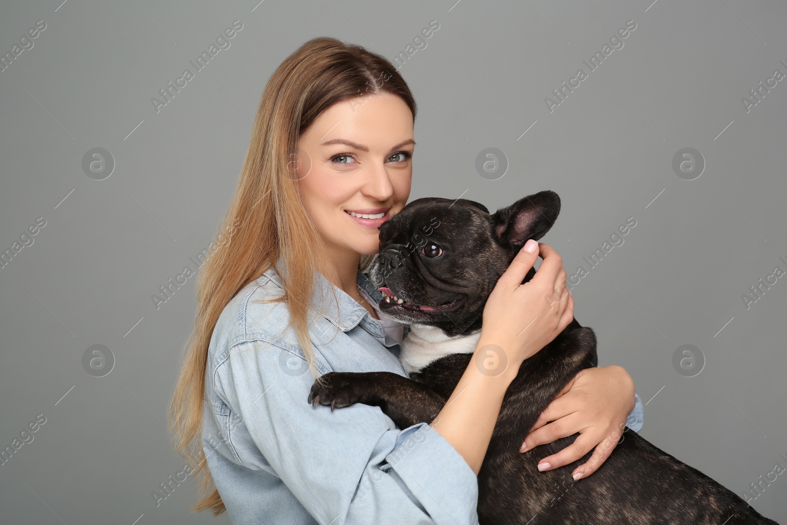 Photo of Portrait of happy woman hugging cute French Bulldog on grey background