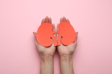 Photo of Woman holding paper cutout of kidneys on pink background, top view