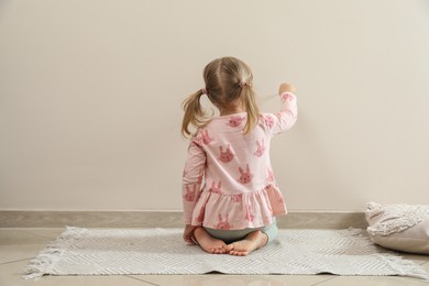 Photo of Little girl drawing on beige wall indoors, back view. Child`s art