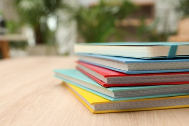 Photo of Stack of colorful planners on wooden table indoors, closeup. Space for text