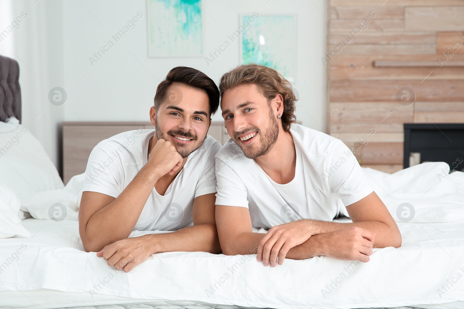 Photo of Happy gay couple lying on bed at home