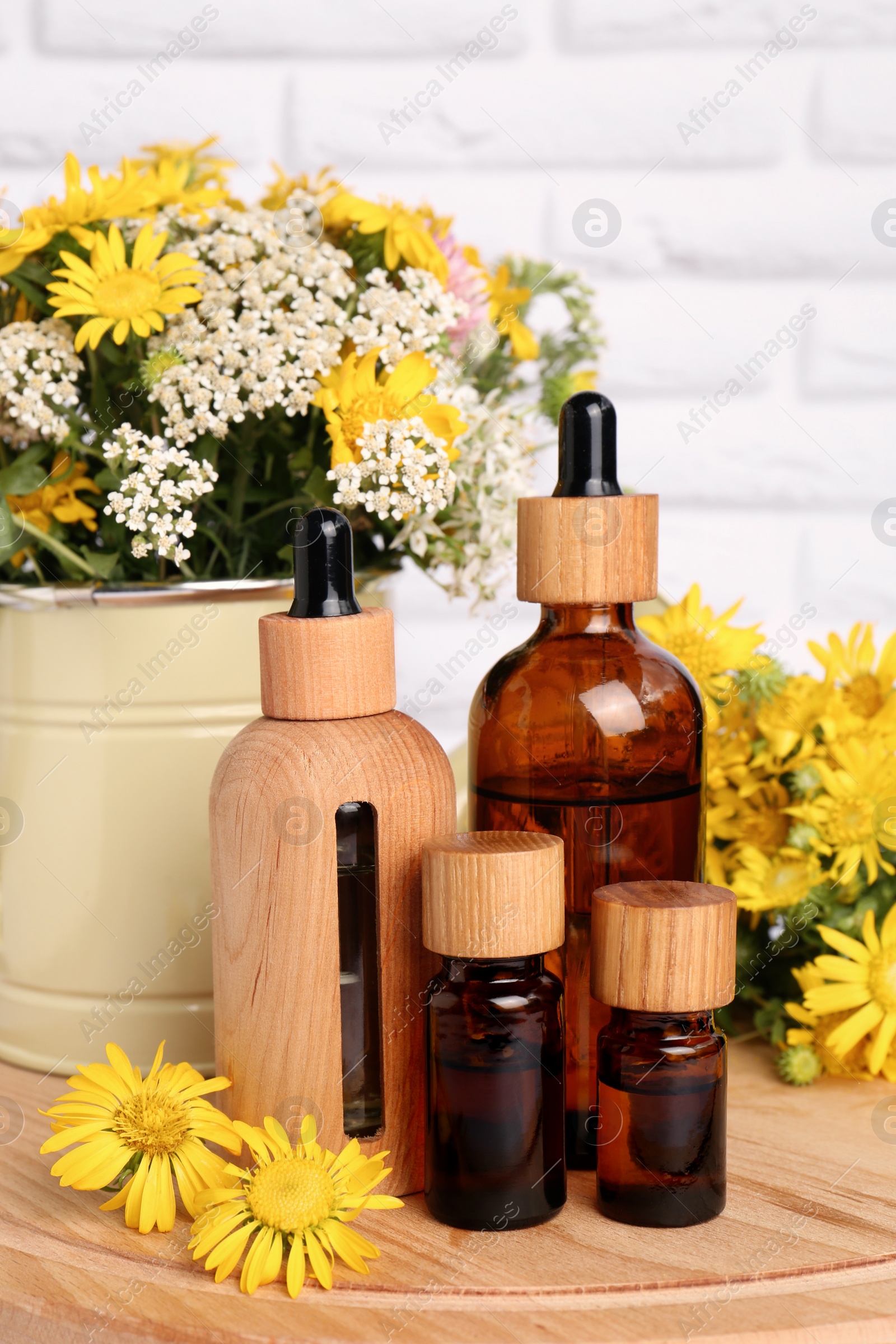 Photo of Bottles of essential oil and different wildflowers on wooden board