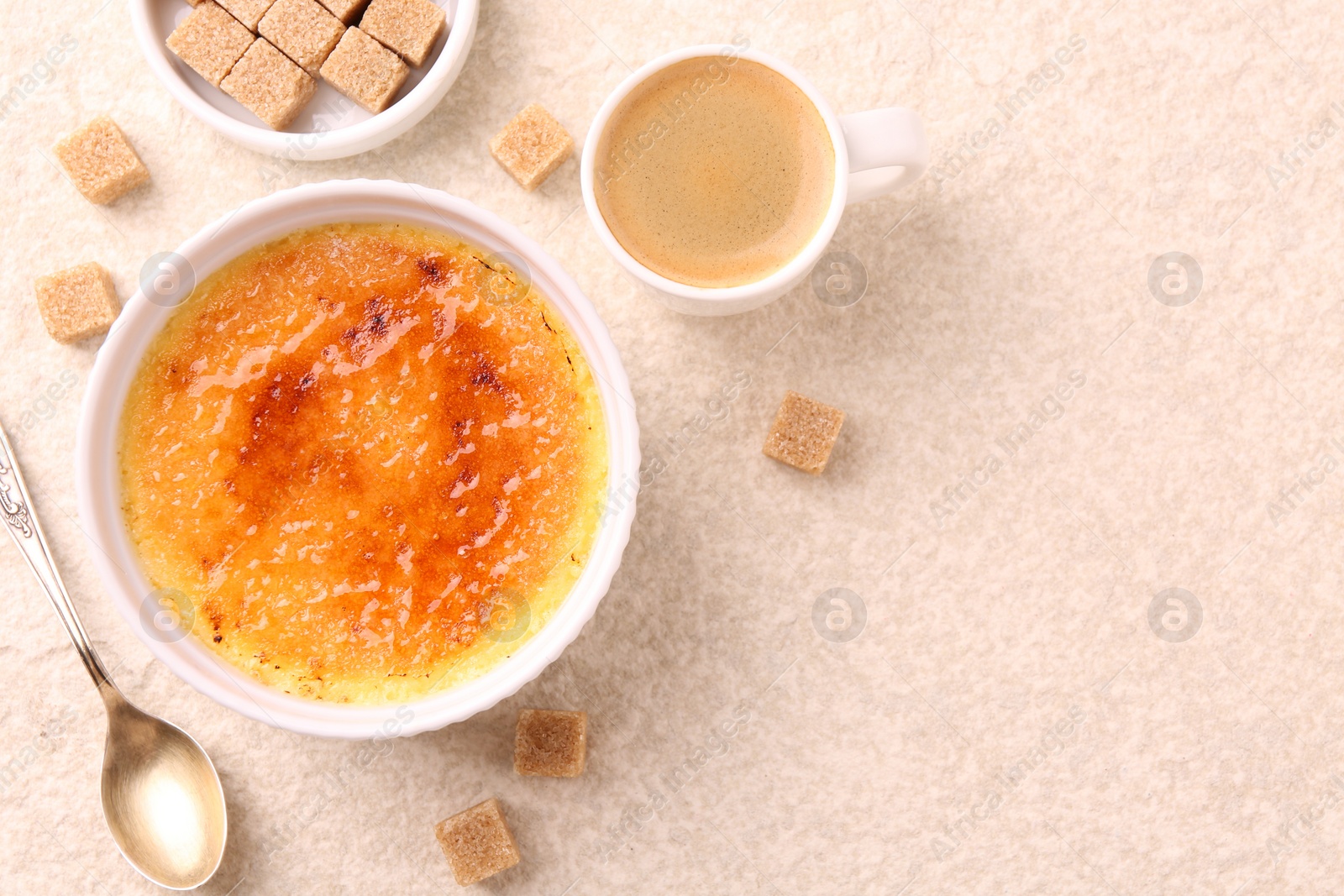 Photo of Delicious creme brulee in bowl, sugar cubes, coffee and spoon on light textured table, flat lay. Space for text