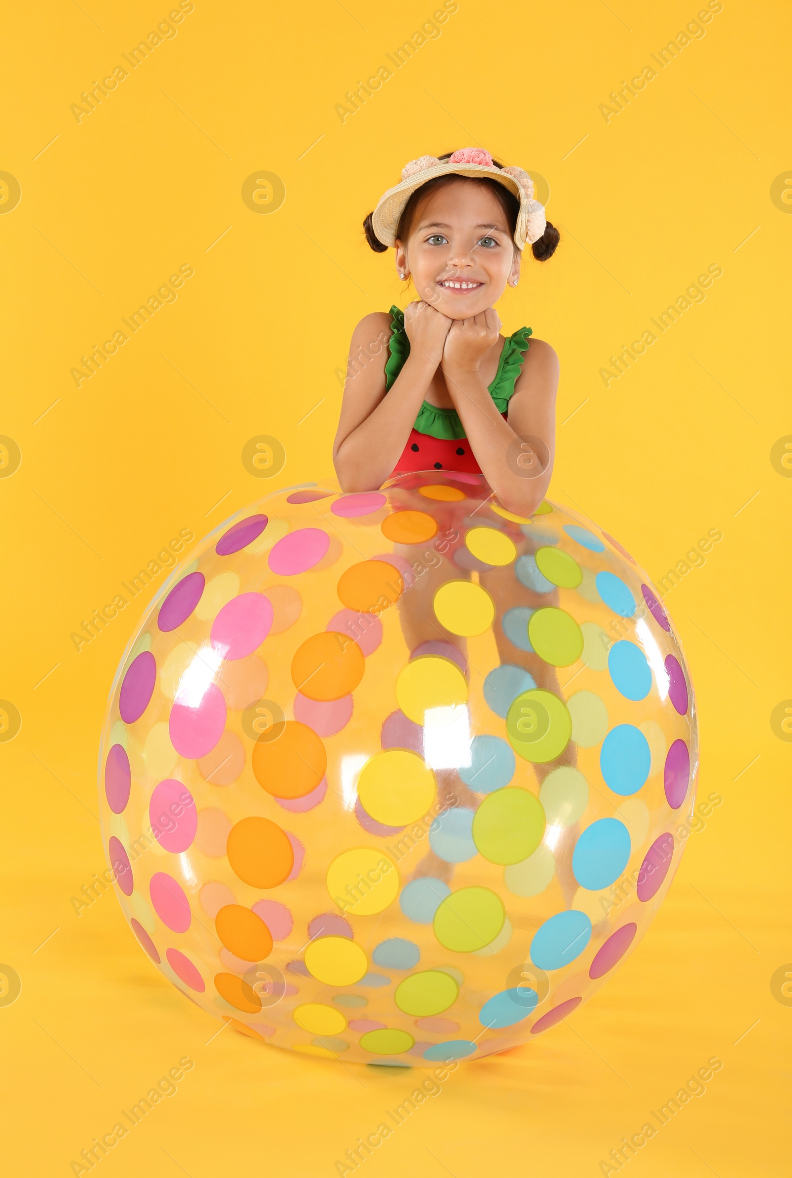 Photo of Cute little child in beachwear with bright inflatable ball on yellow background