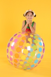 Cute little child in beachwear with bright inflatable ball on yellow background
