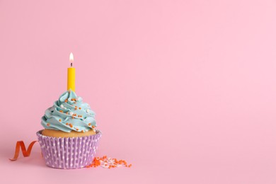 Photo of Birthday cupcake with burning candle, streamer and sprinkles on pink background. Space for text