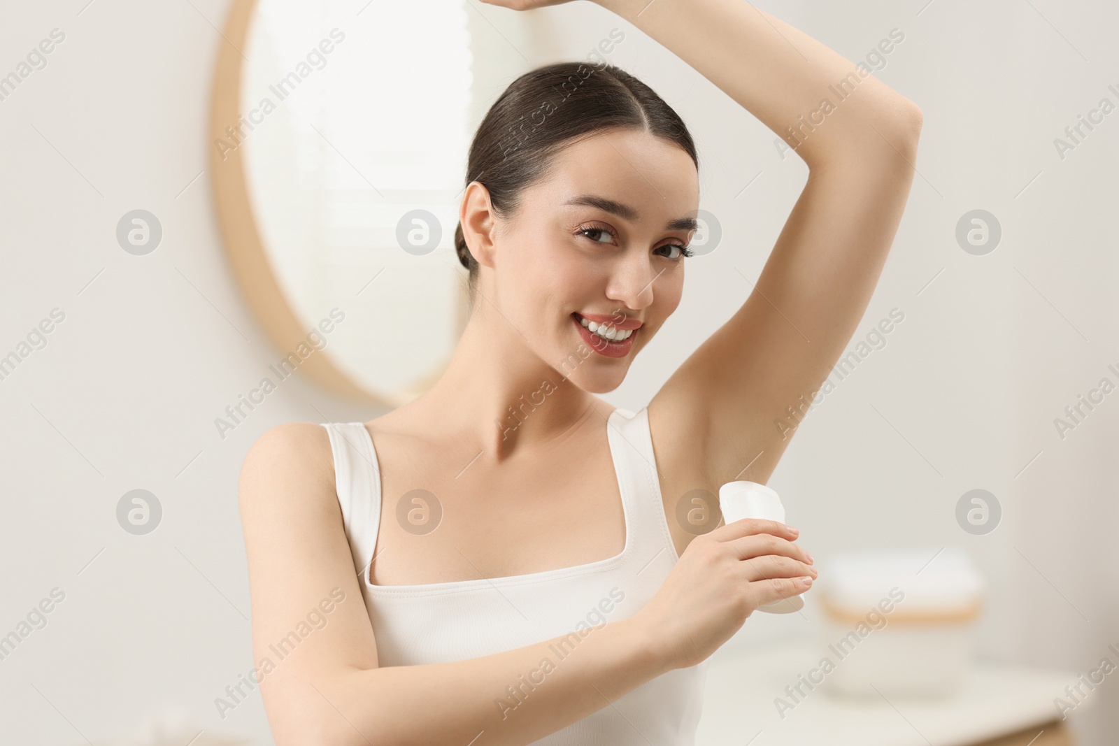 Photo of Beautiful young woman applying deodorant in bathroom