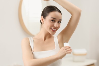 Beautiful young woman applying deodorant in bathroom