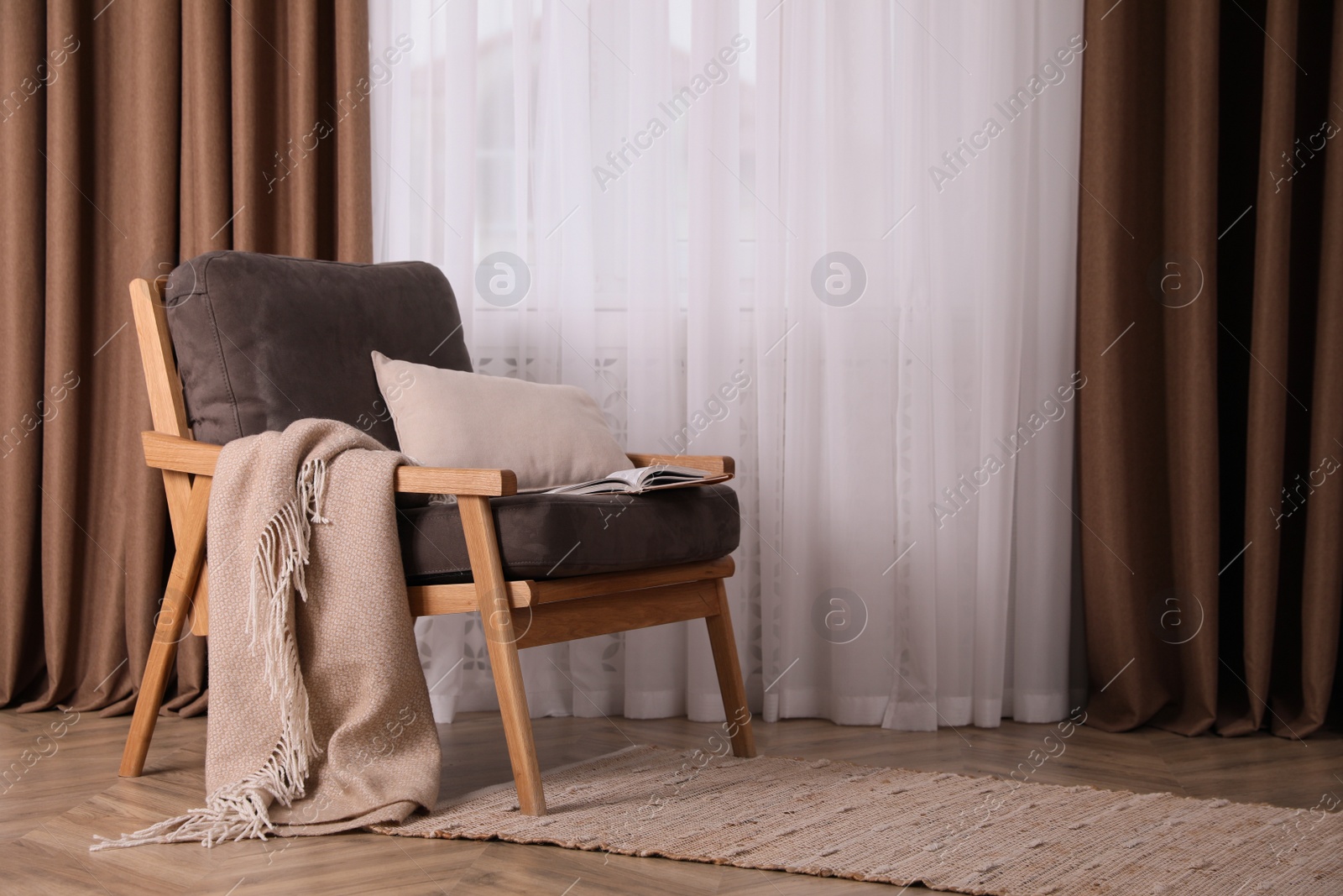 Photo of Comfortable armchair with blanket near window indoors, space for text. Interior design