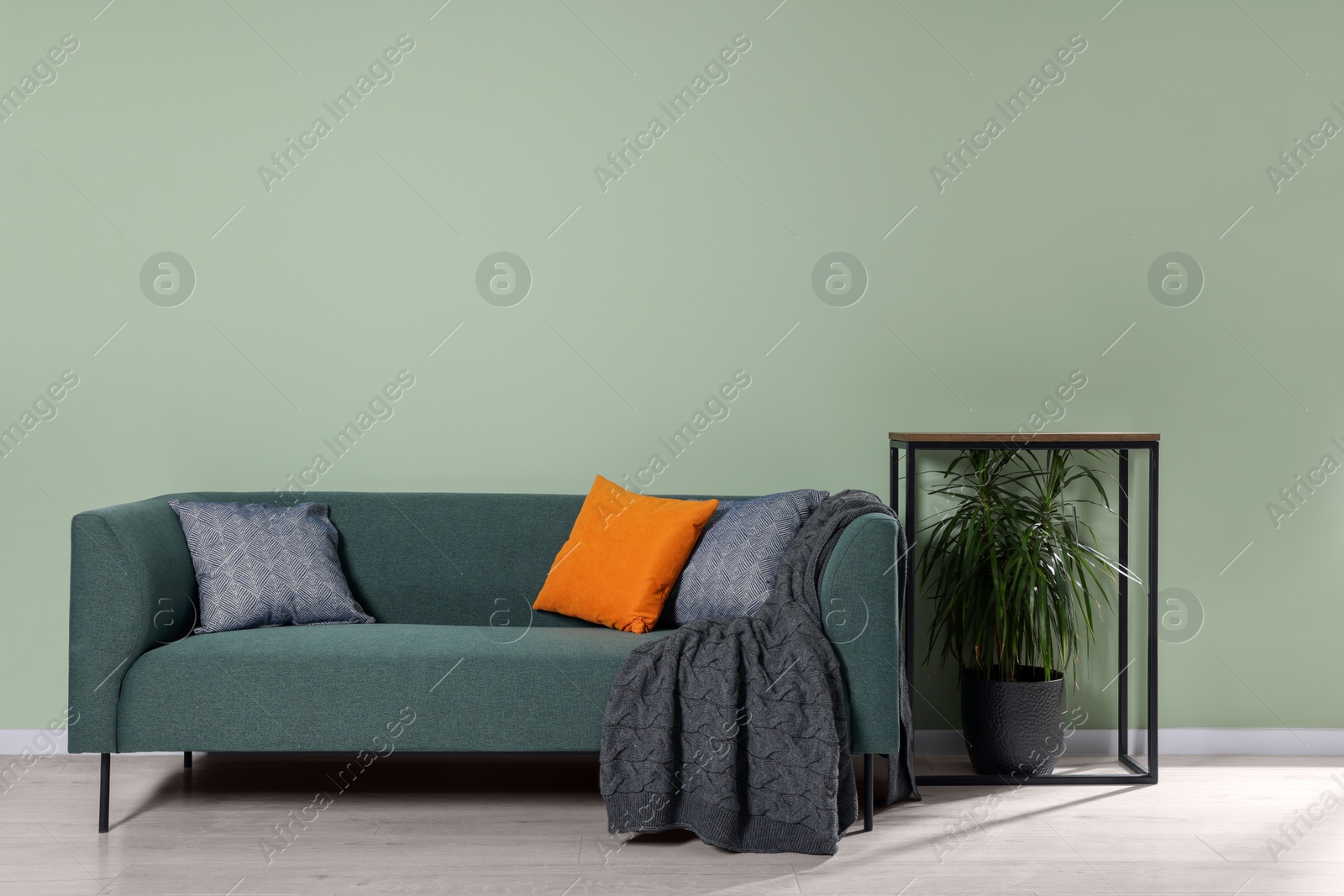 Photo of Comfortable sofa with cushions and blanket near console table indoors. Interior design