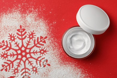 Winter skin care. Hand cream and snowflake silhouette made with artificial snow on red background, top view
