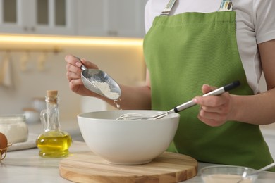 Photo of Making bread. Woman putting flour into bowl at white table in kitchen, closeup