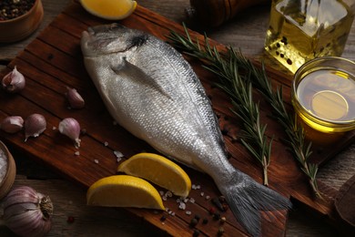 Photo of Raw dorado fish, lemon wedges, spices and oil on wooden table