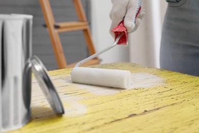 Woman using roller to paint plank with white dye indoors, closeup