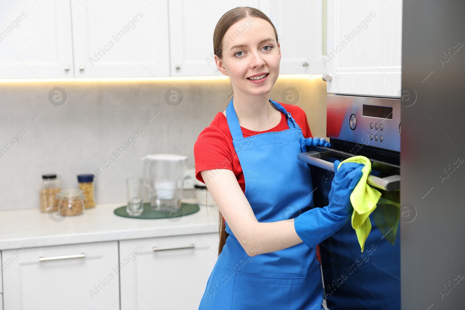 Photo of Woman cleaning electric oven with rag in kitchen