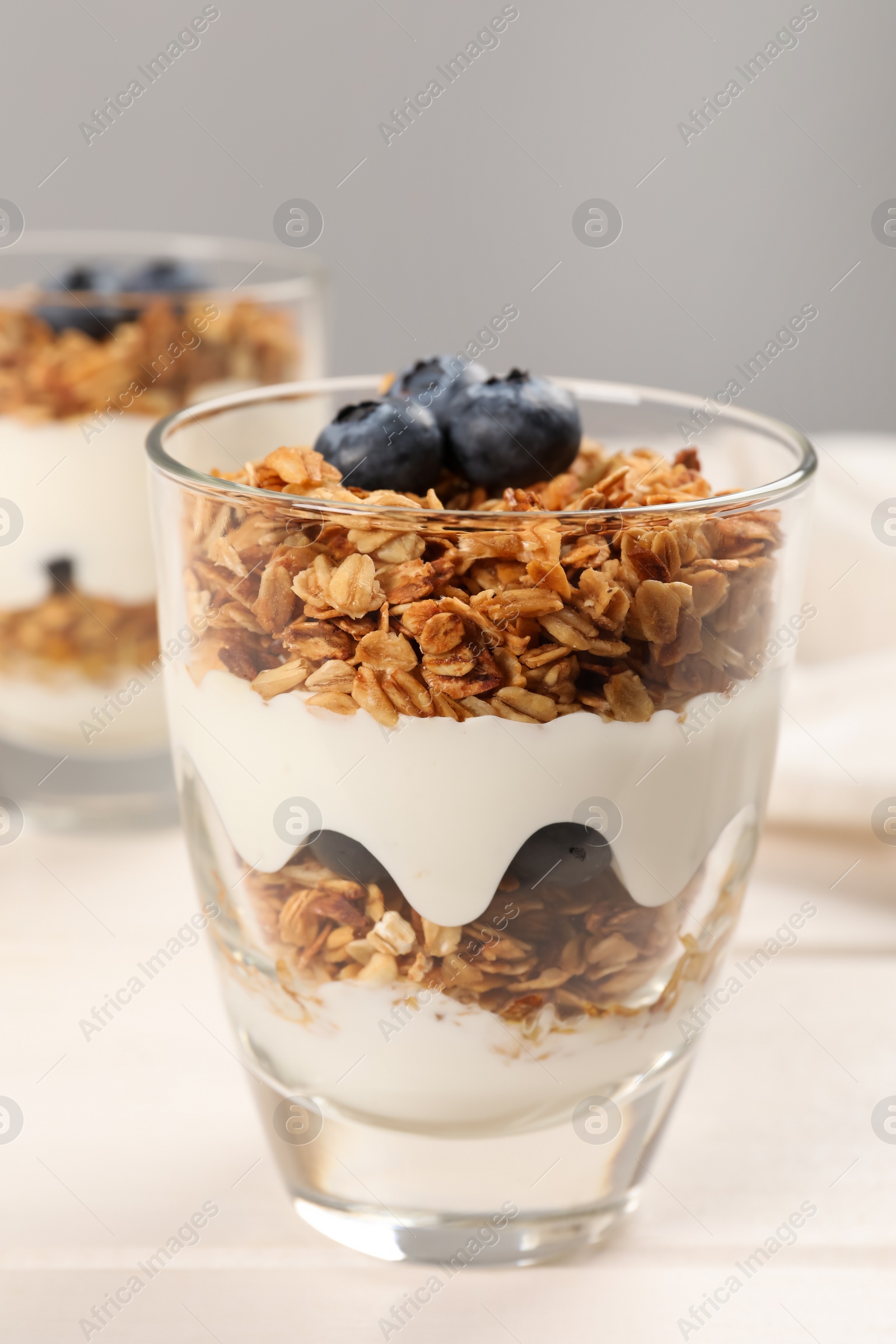 Photo of Glass of tasty yogurt with muesli and blueberries served on white wooden table
