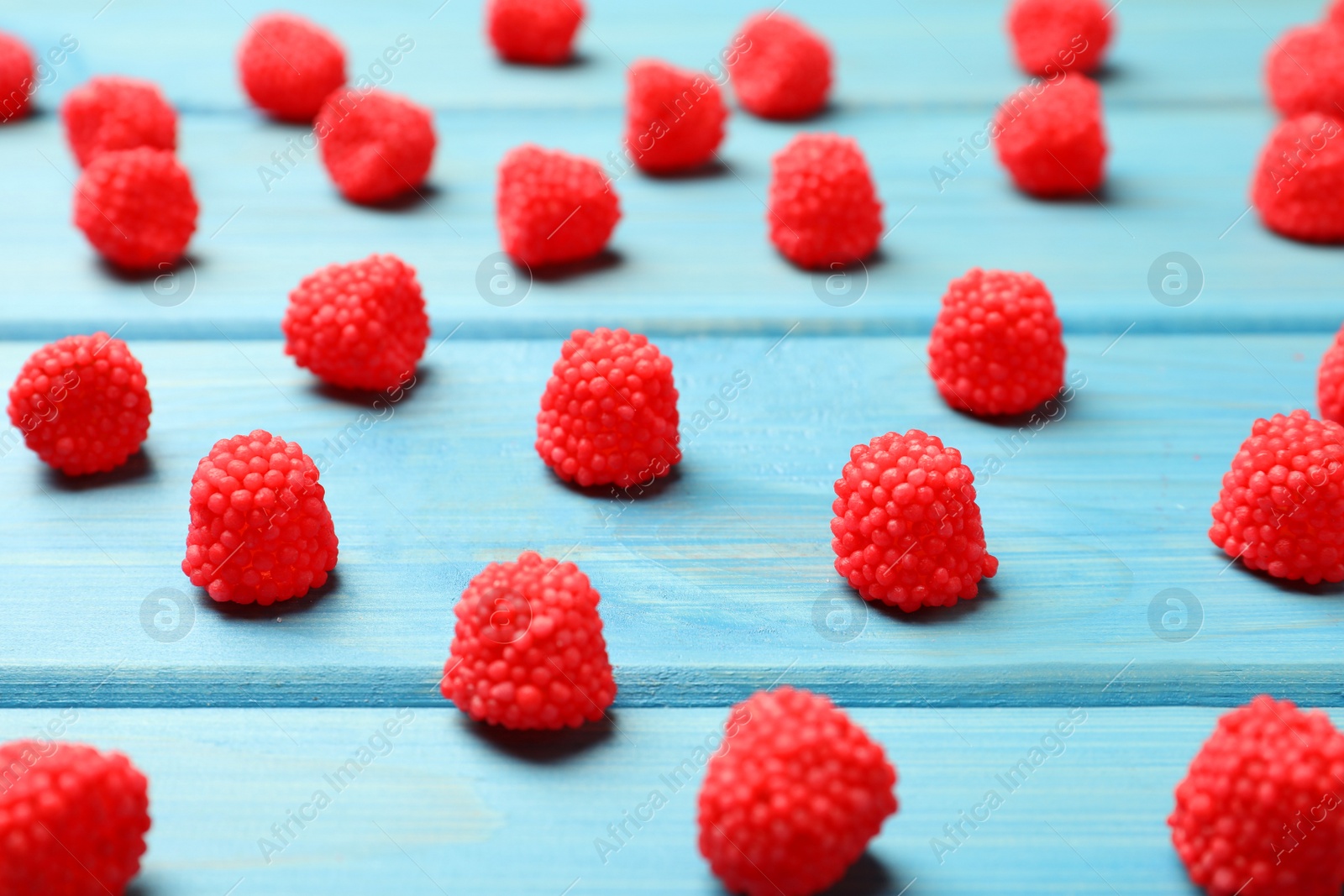 Photo of Delicious gummy raspberry candies on light blue wooden table