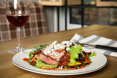 Photo of Delicious salad with roasted meat and vegetables served on wooden table indoors. Space for text