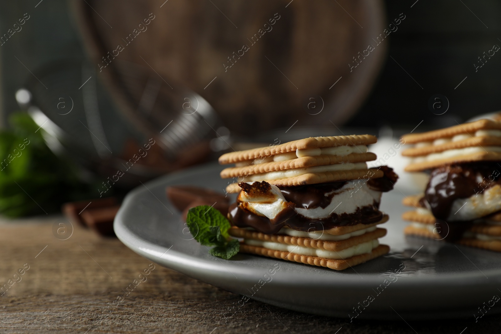 Photo of Delicious marshmallow sandwiches with crackers and chocolate on wooden table, closeup