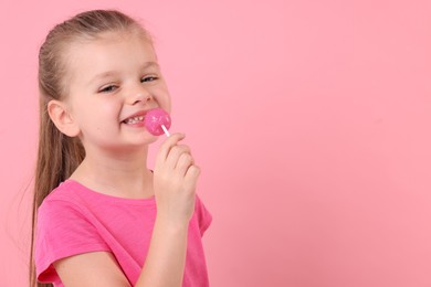 Photo of Happy little girl licking lollipop on pink background, space for text