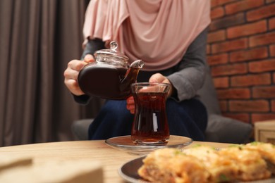 Photo of Woman pouring delicious Turkish tea from teapot into cup at wooden table, closeup