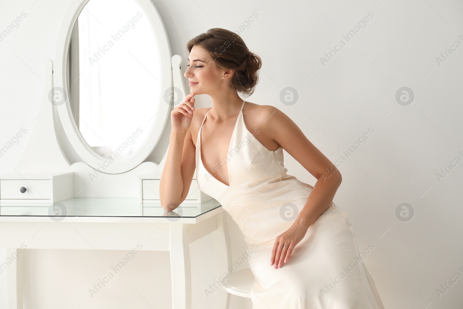 Photo of Young bride in beautiful wedding dress near mirror indoors
