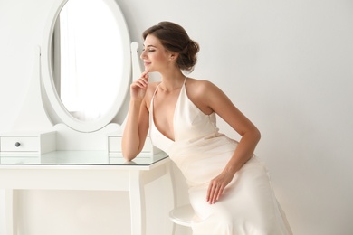 Young bride in beautiful wedding dress near mirror indoors