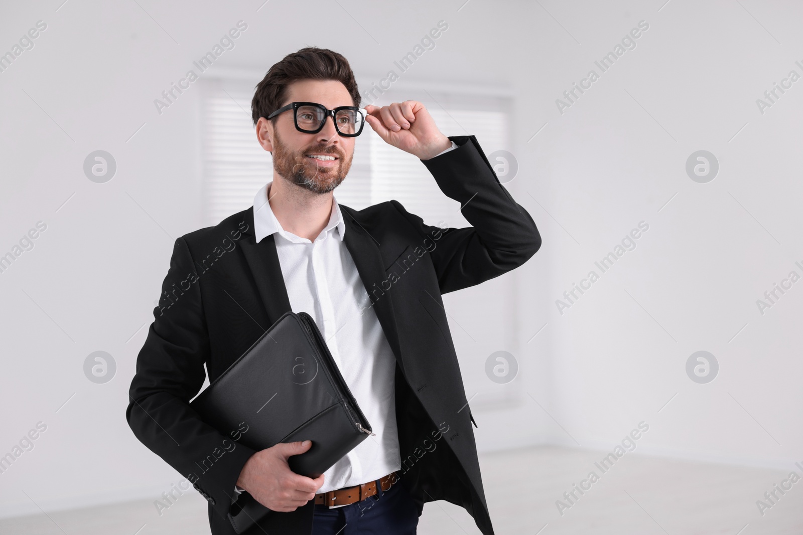 Photo of Happy real estate agent with leather portfolio indoors. Space for text