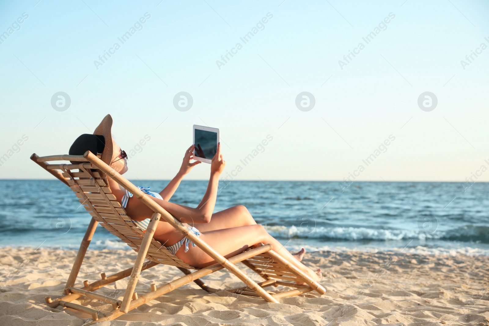 Photo of Young woman with tablet relaxing in deck chair on beach