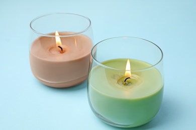 Burning wax candles in glass holders on light blue background