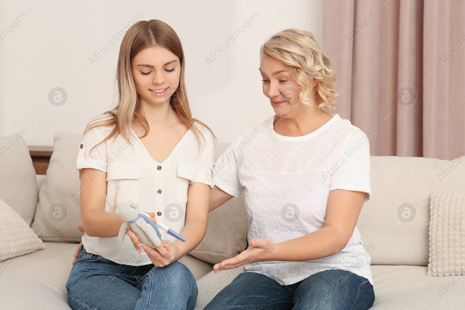 Photo of Young woman with toy bunny showing her mother pregnancy test at home. Grandparent reaction to future grandson