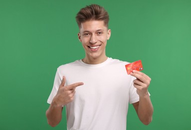 Photo of Happy man pointing at credit card on green background