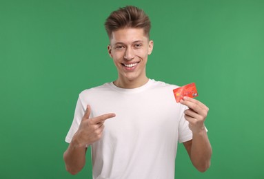 Happy man pointing at credit card on green background