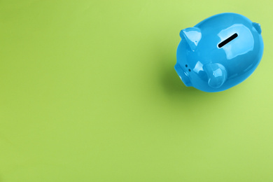 Photo of Blue piggy bank on green background, top view. Space for text