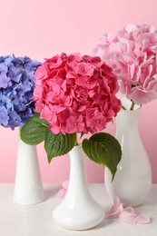 Photo of Beautiful bright hortensia flowers on white wooden table against pink background, closeup