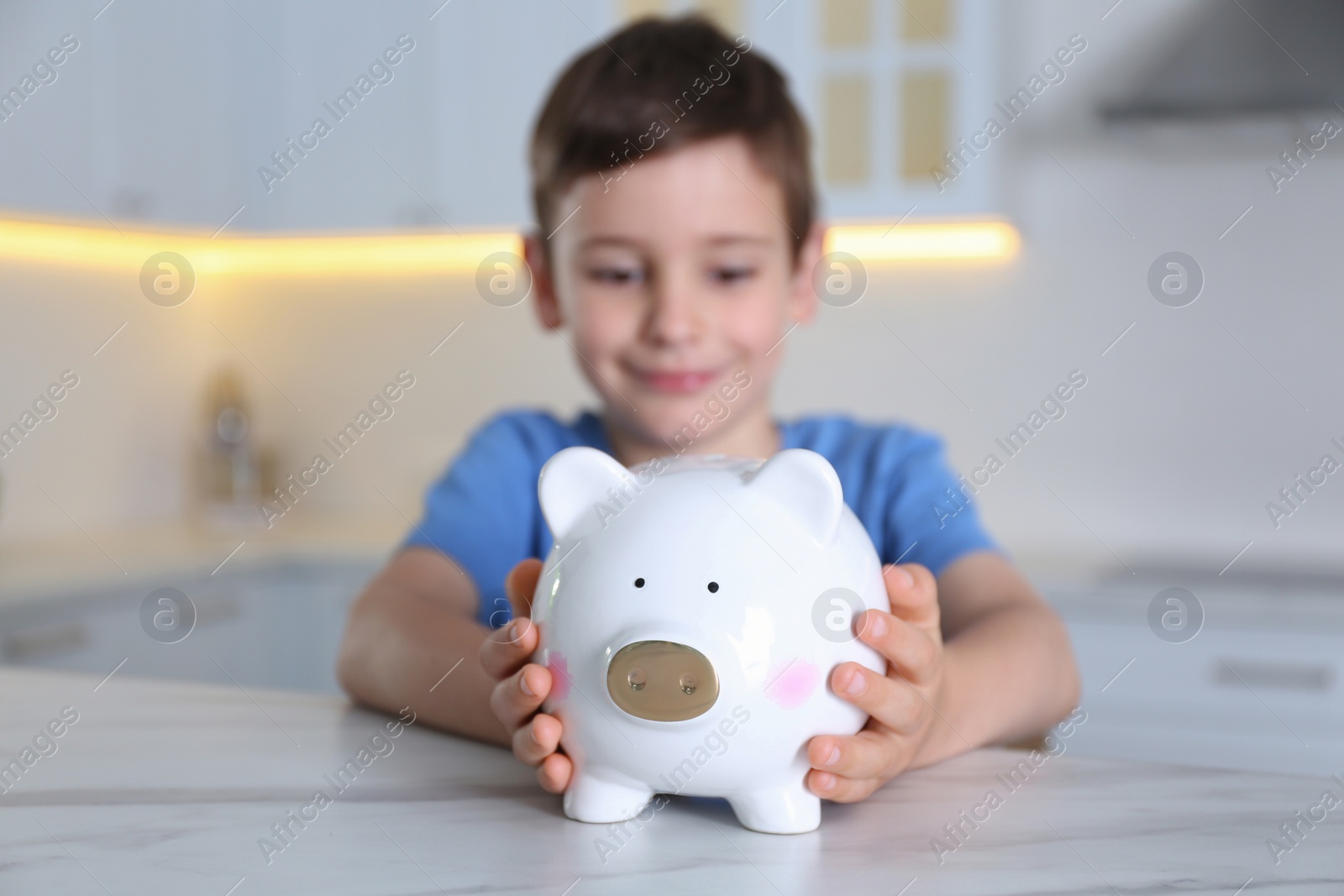 Photo of Little boy with piggy bank at marble table indoors