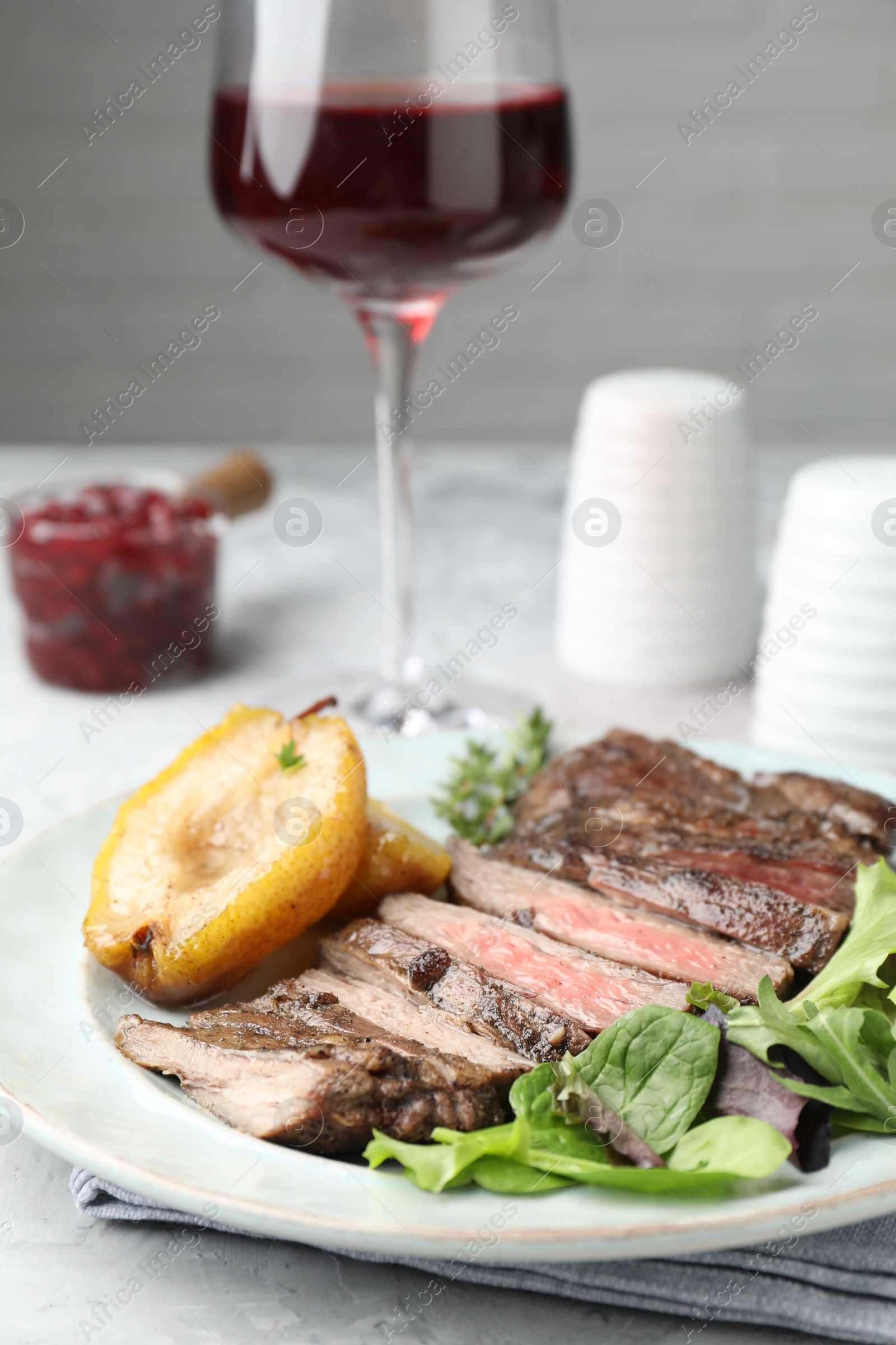 Photo of Delicious roasted beef meat, caramelized pear and greens served on table, closeup