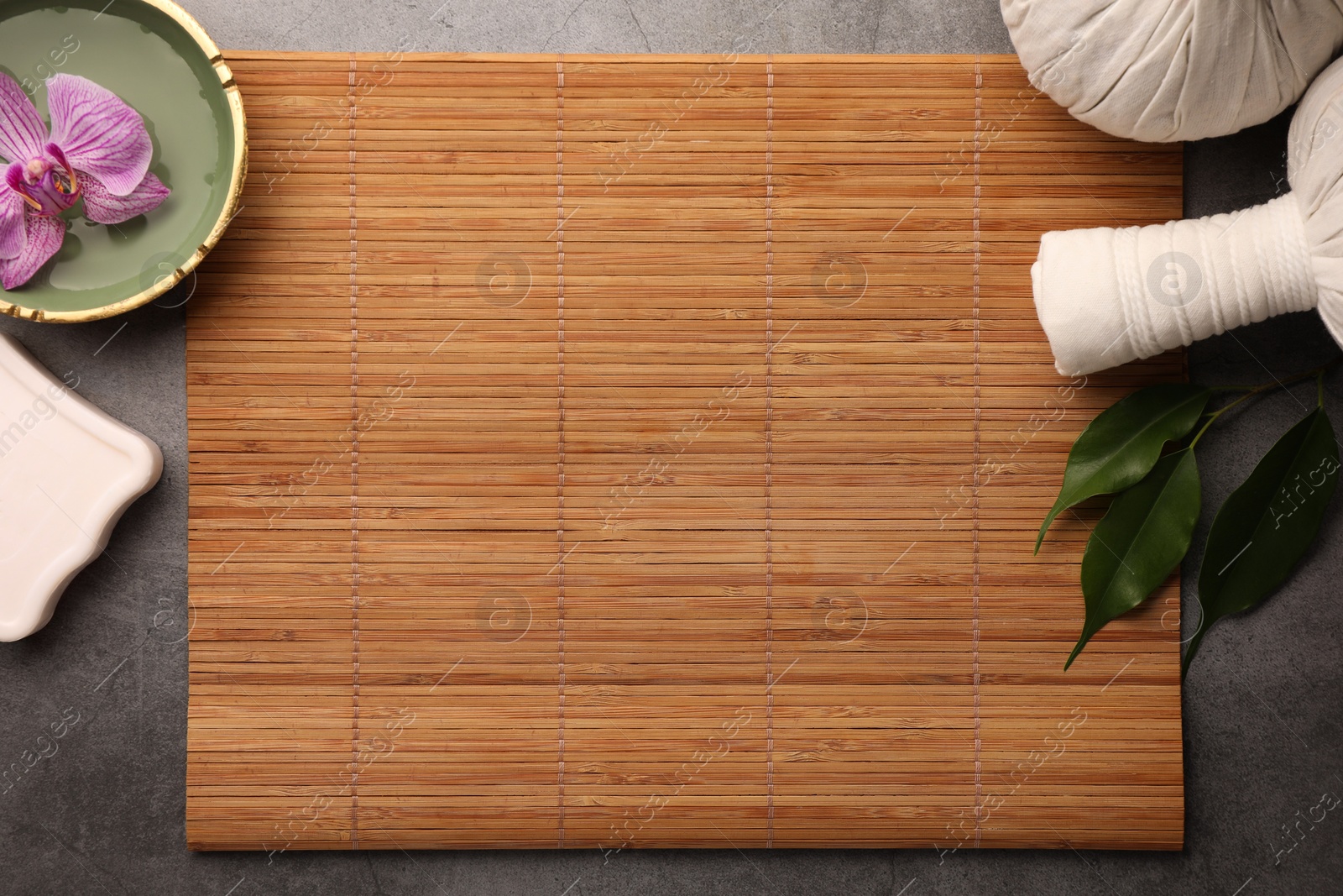 Photo of Flat lay composition with bamboo mat, spa herbal pouches and bowl with orchid flower on grey table. Space for text