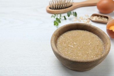 Homemade hair mask in bowl and ingredients on white wooden table. Space for text