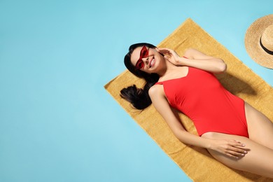 Photo of Young woman in stylish swimsuit on beach towel against light blue background. Space for text