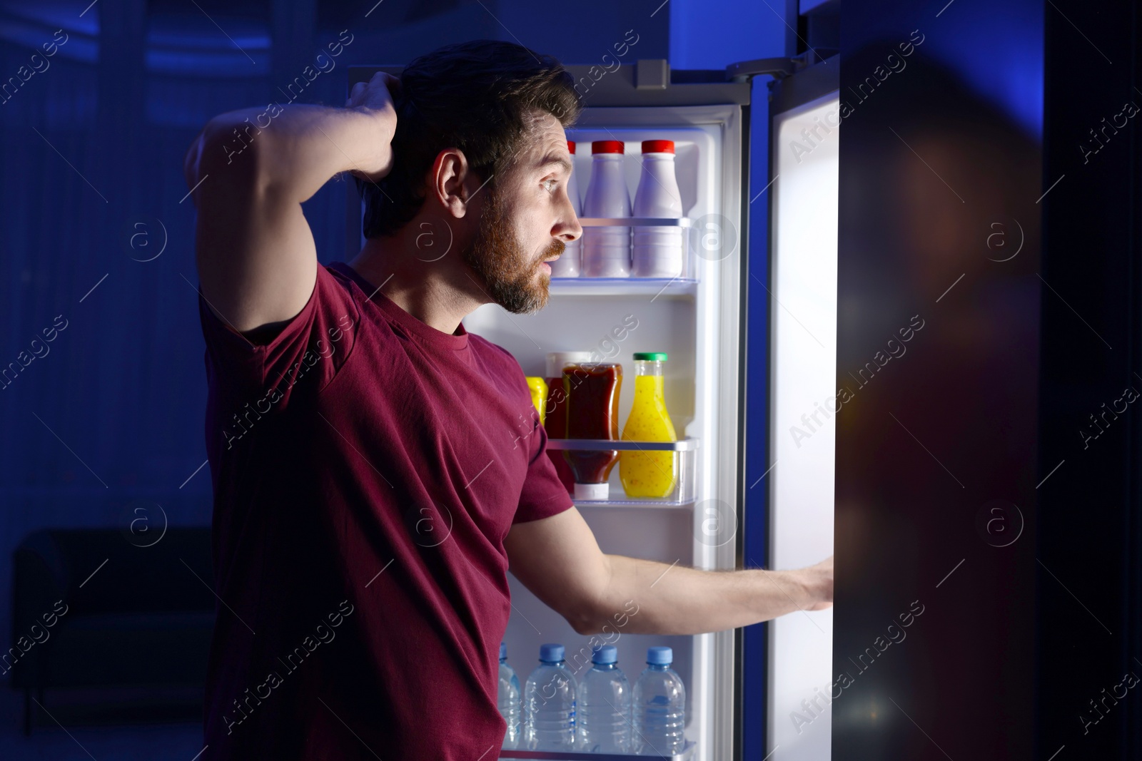 Photo of Man choosing food from refrigerator in kitchen at night. Bad habit