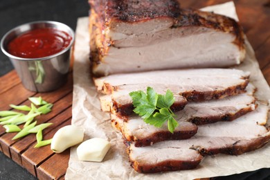 Photo of Pieces of baked pork belly served with sauce and parsley on table, closeup