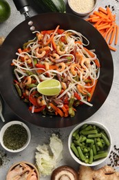 Shrimp stir fry with noodles and vegetables in wok surrounded by ingredients on grey table, flat lay